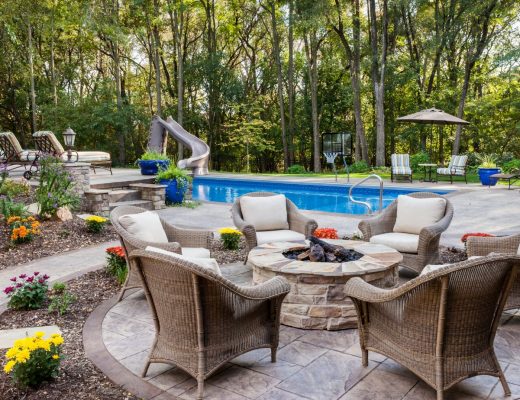 beige patio chairs surround a fire pit in the foreground with a swimming pool in the background