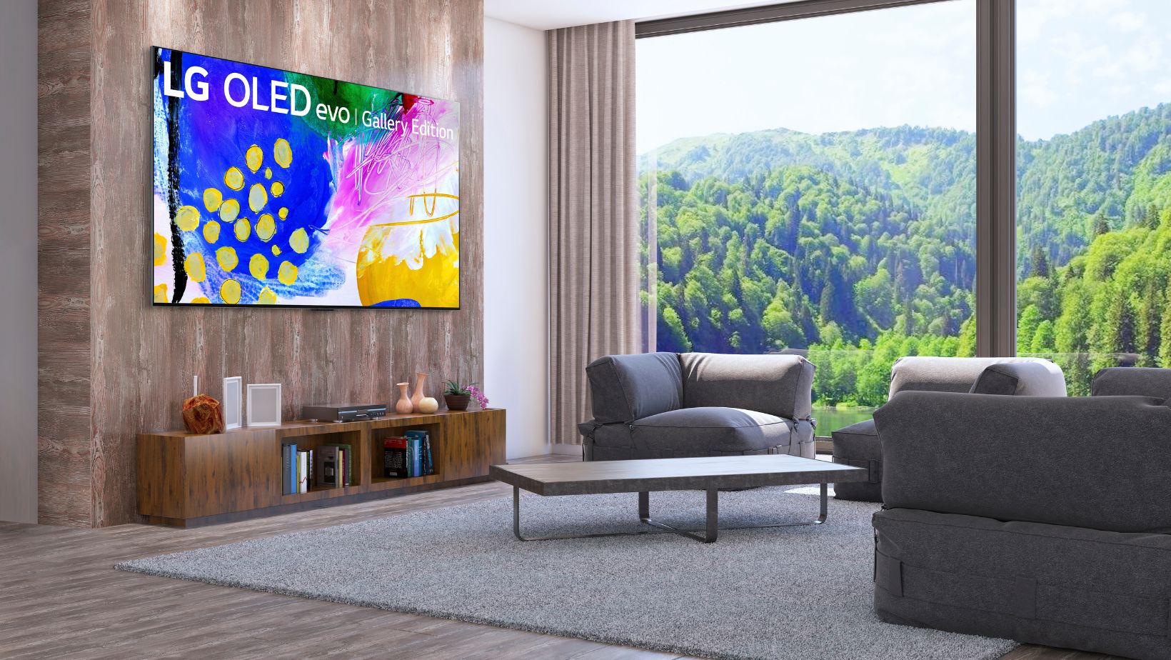 The 97" LG OLED evo TV is mounted on a wall. Underneath the TV is an entertainment console with a media player and decorative objects on it. The TV is across from a grey sectional and a coffee table.