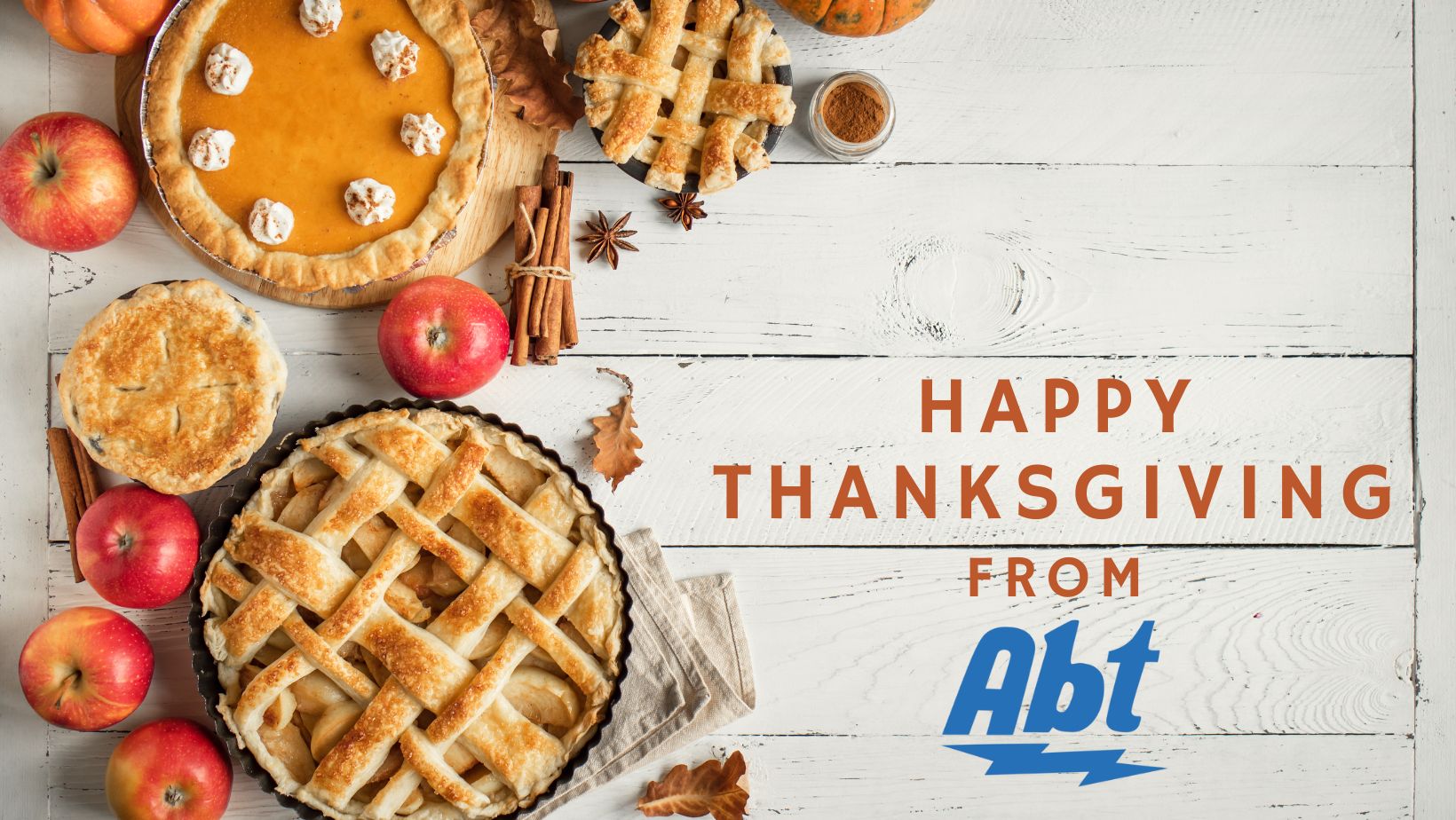 Burnt orange text reads "happy Thanksgiving from" with the blue Abt logo underneath. Next to the text are several pies, apples and cinnamon sticks