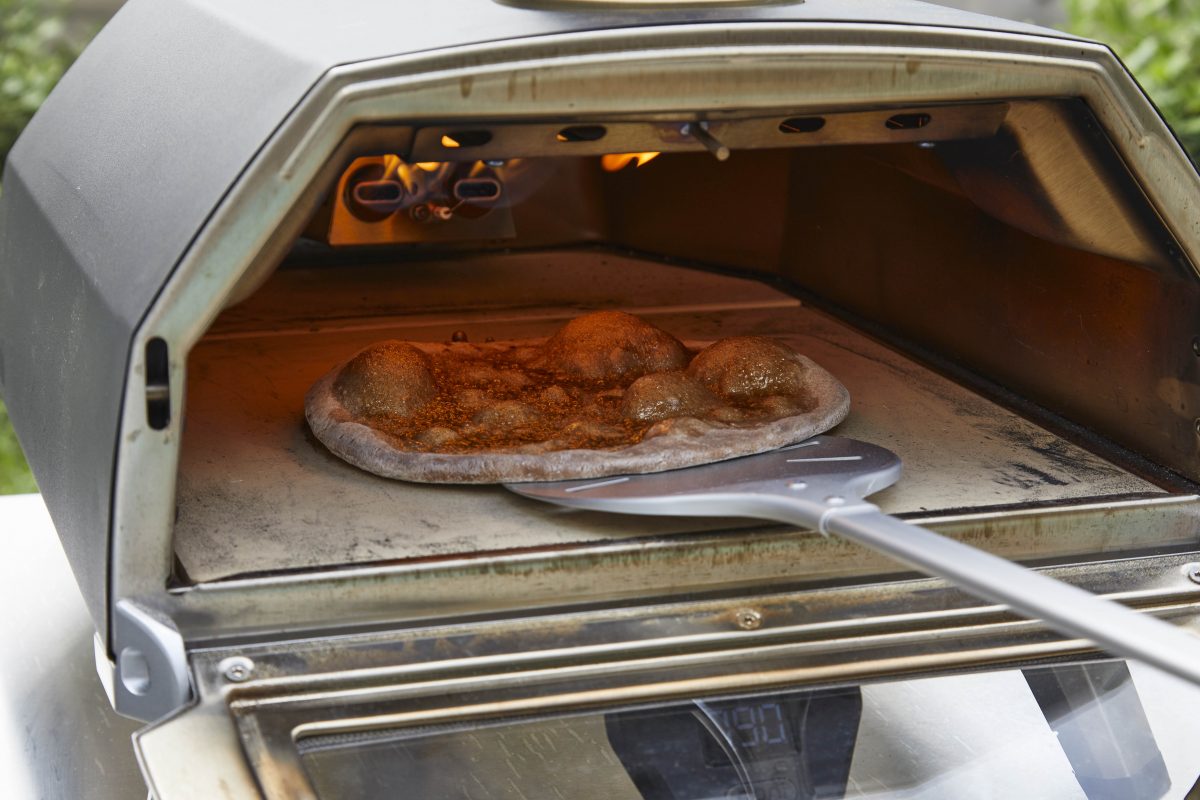 Pizza being slid into a pizza oven on a silver pizza peel