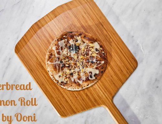 dessert pizza with icing and candy ginger on top sits on a wooden pizza peel. The pizza peel sits on a marble surface
