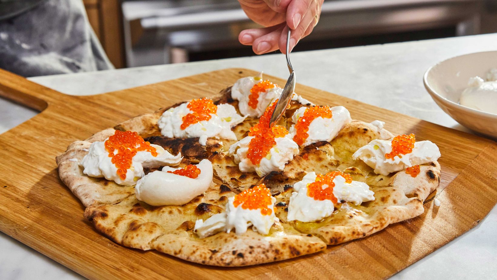 closeup of pizza crostini with burrata and orange trout roe on a wooden pizza peel