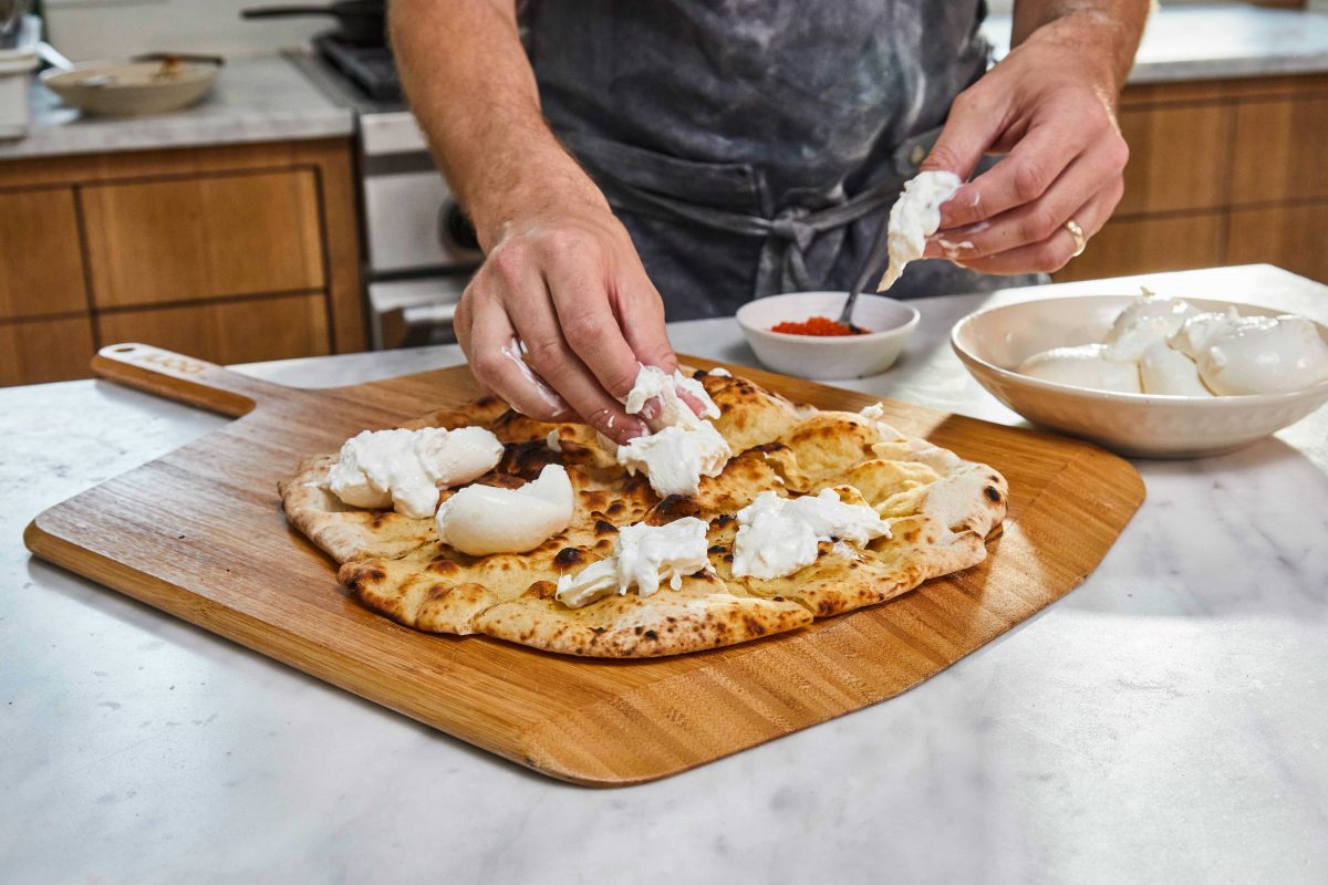Hands tearing burrata and placing on a pizza crostini