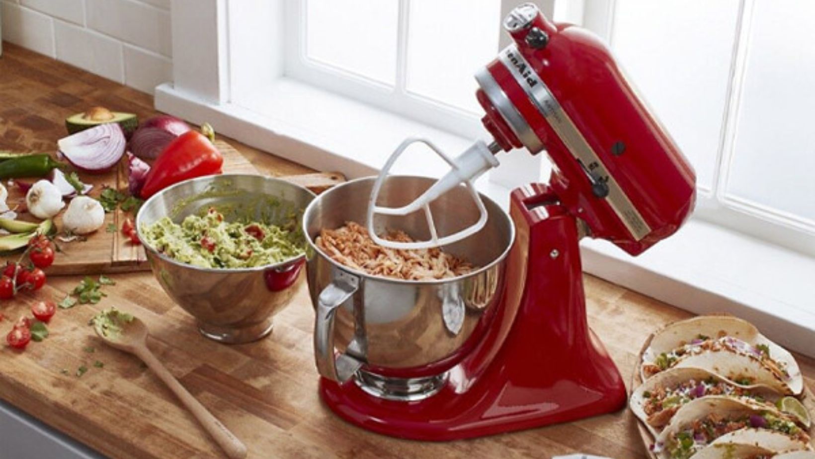 red KitchenAid stand mixer on a wooden counter next to a plate of tacos