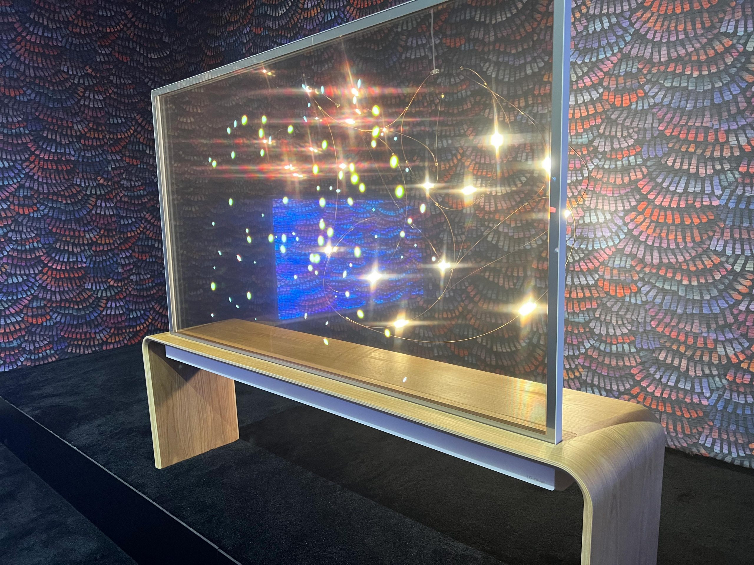 LG OLED T TV on display with patterned wallpaper visible through the transparent screen