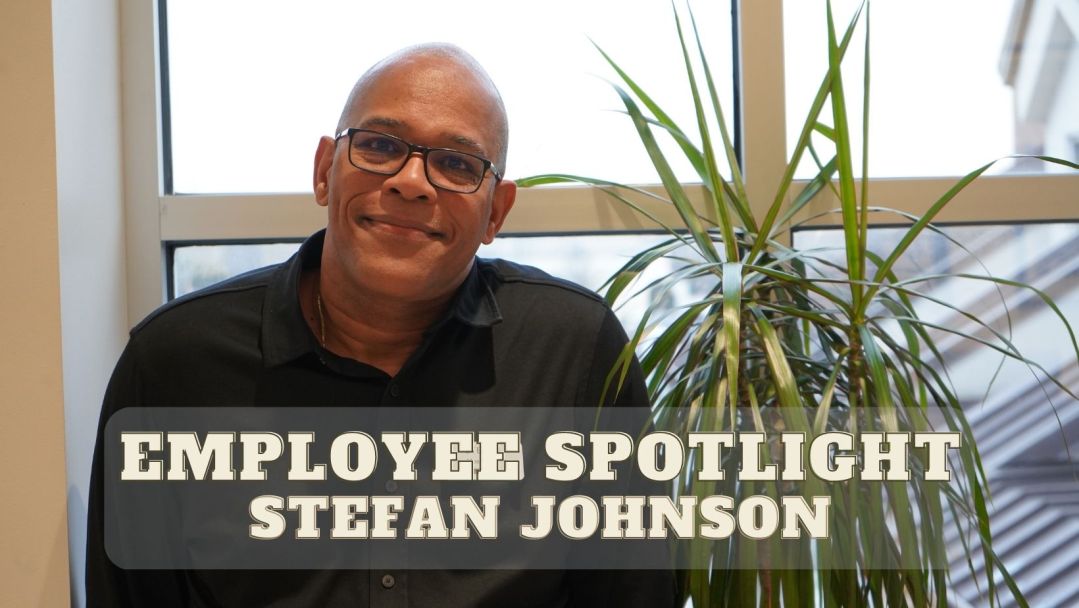 Stefan Johnson, HR Manager at Abt, stands beside a fern, smiling. They are in front of a window. The words "Employee Spotlight! Stefan Johnson" are on the image.