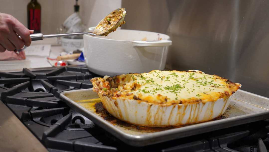 Chef susan scooping a serving of shepherd's pie from the casserole dish atop a BlueStar range