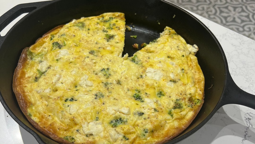 A Broccoli and Feta Frittata in a cast iron pan with a slice taken out.