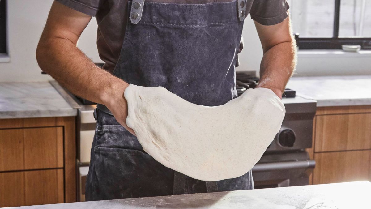 Person In Kitchen Stretching Pizza Dough