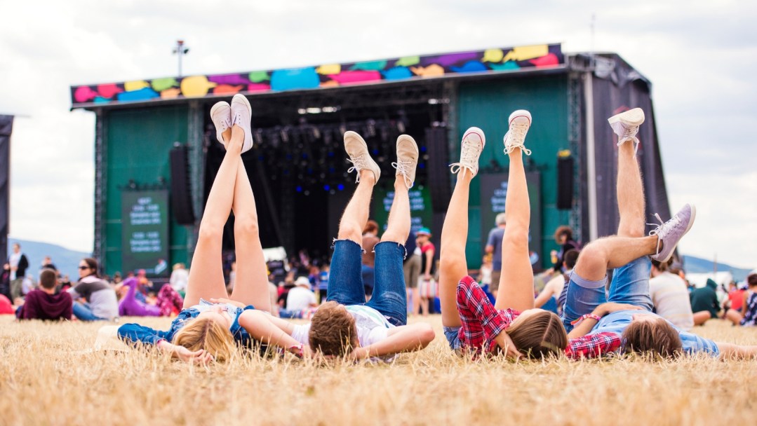 Four friends laying in the grass in front of an outdoor concert stage