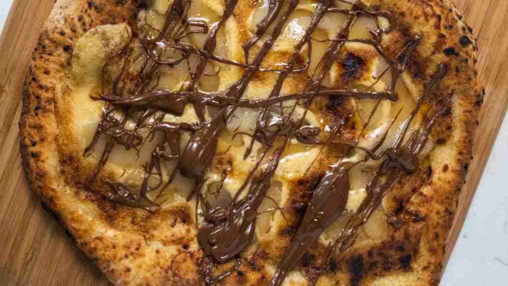 A Pizza on a wooden board covered with poached pears and swirls of Nutella