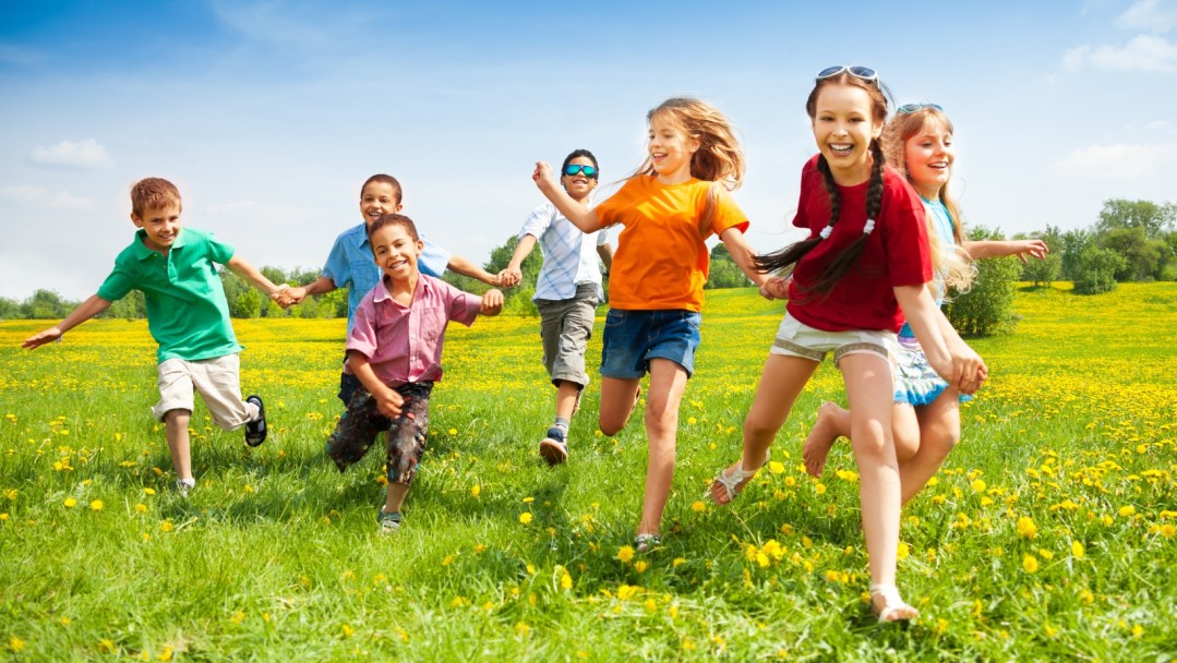 Children running and laughing together in a sunny, green field of grass.