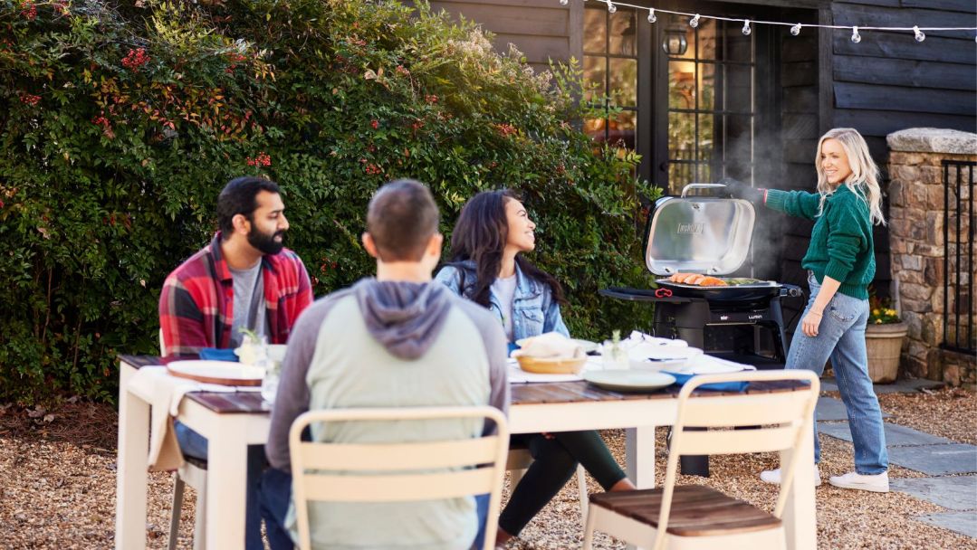 woman grilling next to three people sitting at a patio table