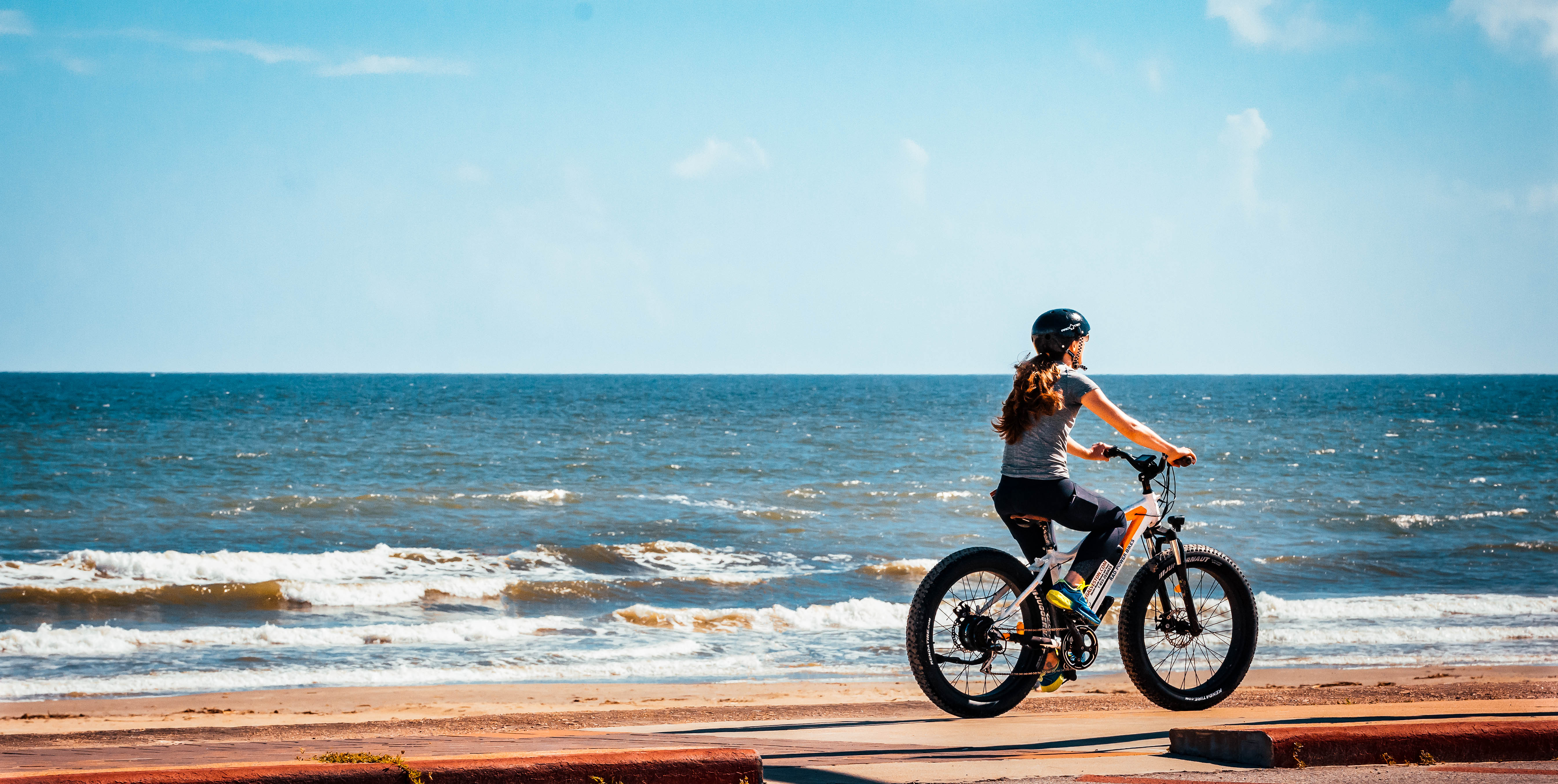 Woman riding e-bike on the beach with waves crashing in.