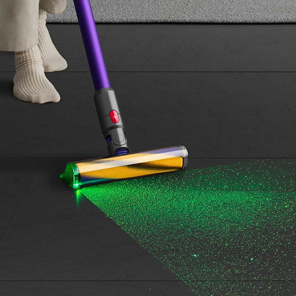 The Dyson Gen5 Detect stick vacuum cleaning the floor, with a green light illuminating the dust particles in front of it.