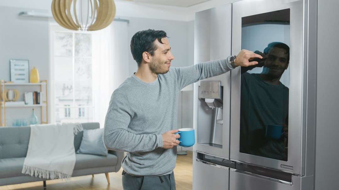Man standing in kitchen with coffee using his smart fridge.