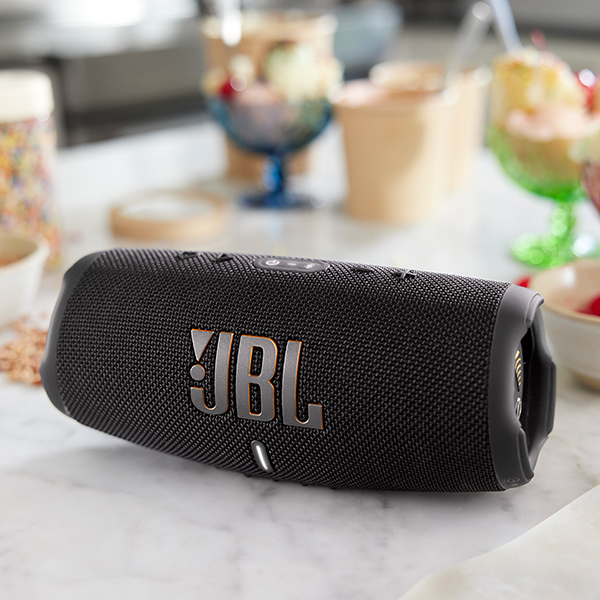 A black JBL wireless speaker laying on its side on a countertop, with food in the background.