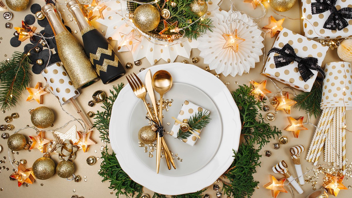 A gold and black holiday party table with a plate and silverware, covered in lights, ornaments and other decor