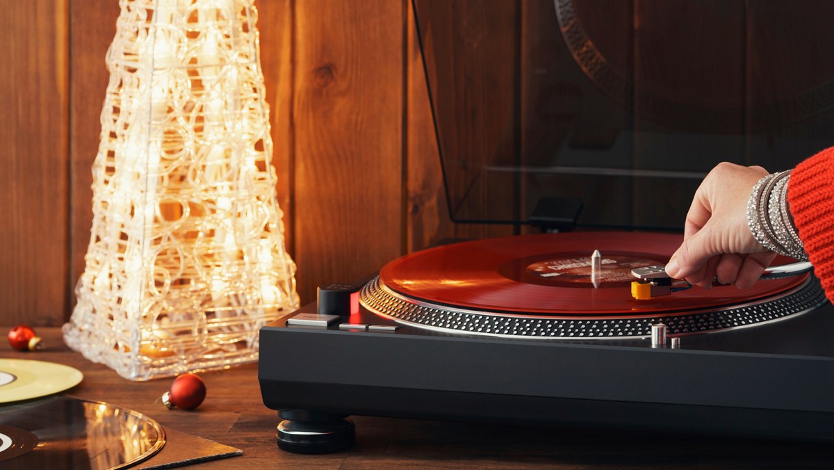 Someone putting the needle on the record using a turntable, next to holiday decorations
