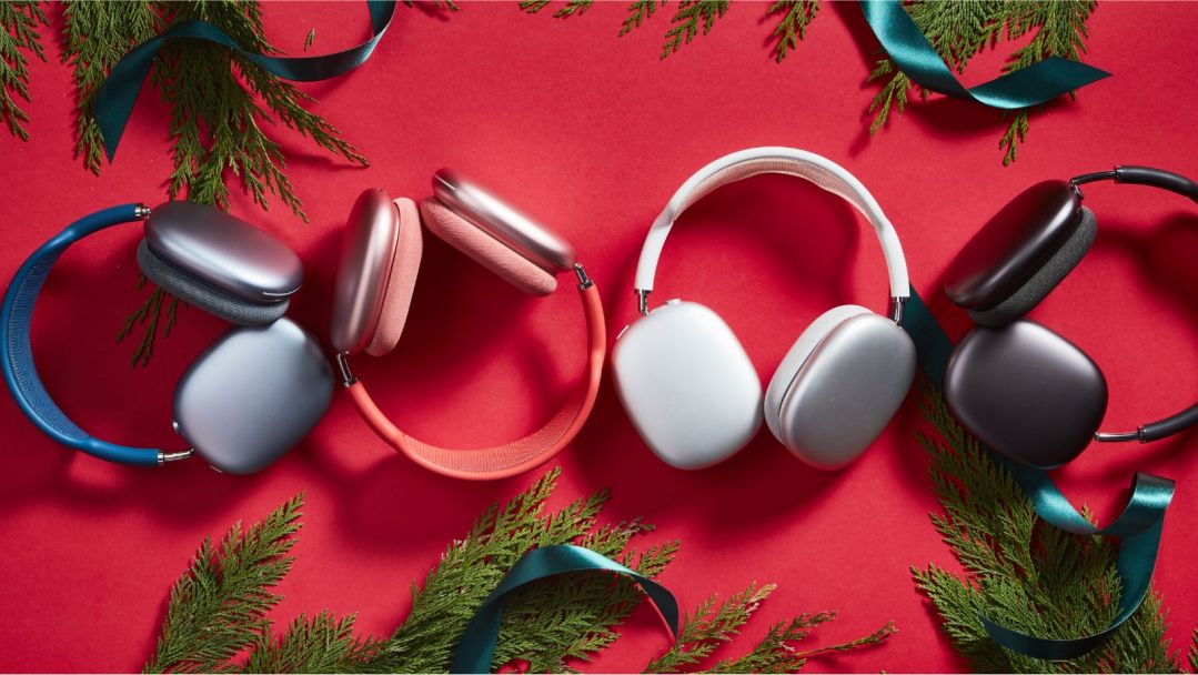 A line of AirPods Max Headphones displayed with holiday greens