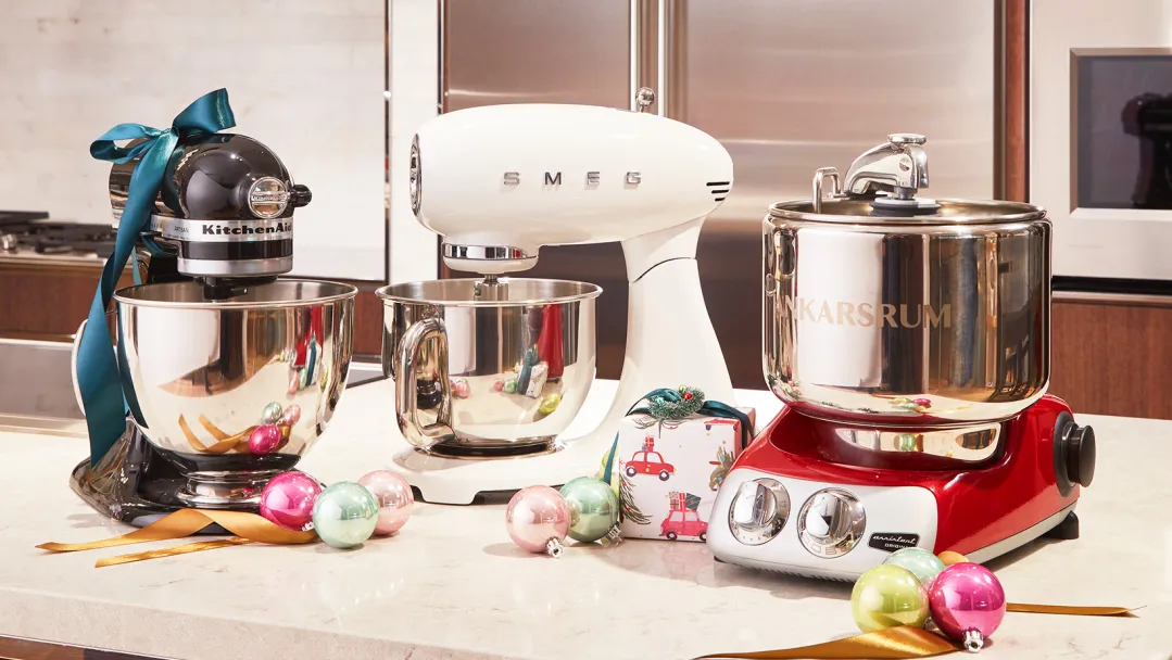 Three stand mixers sitting next to each other on a counter covered in holiday decor