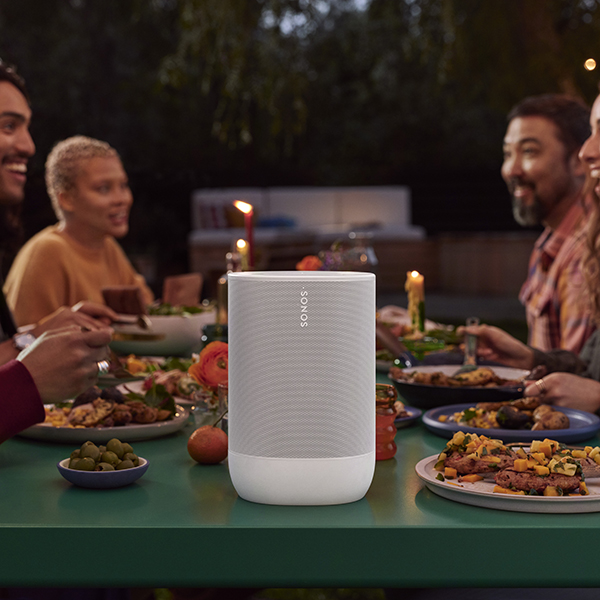 A white wireless speaker sitting on a holiday table with people eating dinner around it.