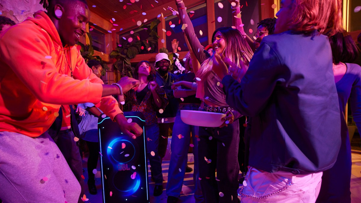 A group of people dancing at a party with confetti in the air and a large JBL speaker at the center