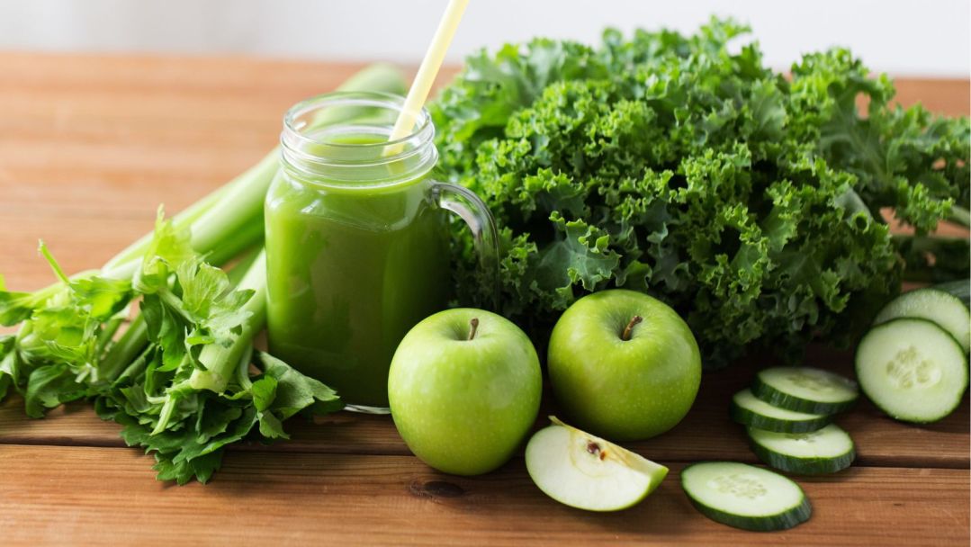A cup of green juice surrounded by green apples, kale, celery and other produce
