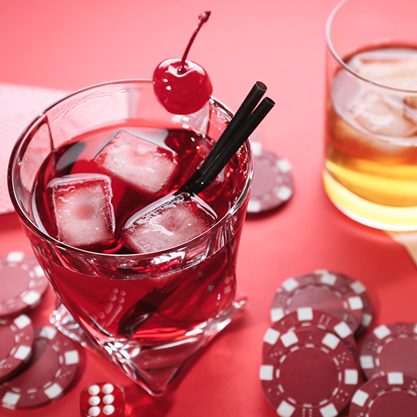 A red cocktail surrounded by poker chips and dice from a game room