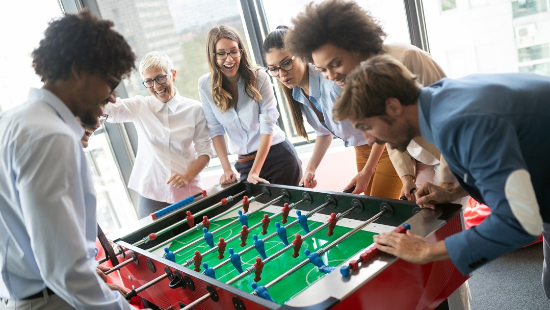 A group of friends in a game room gathered around a foosball table playing excitedly