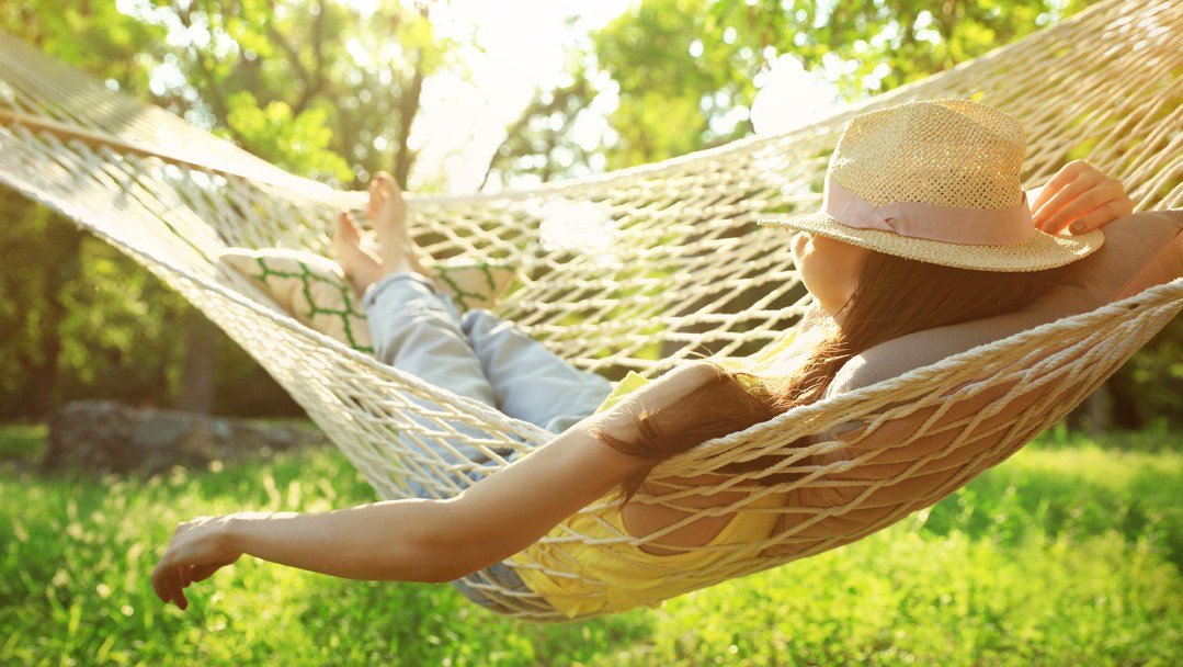 A girl laying in a woven hammock outside with a hat covering her face