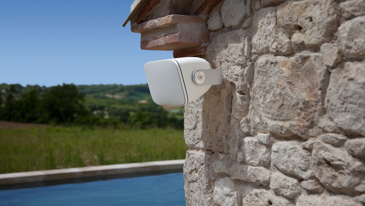 A white outdoor speaker mounted to the exterior stone wall of a home