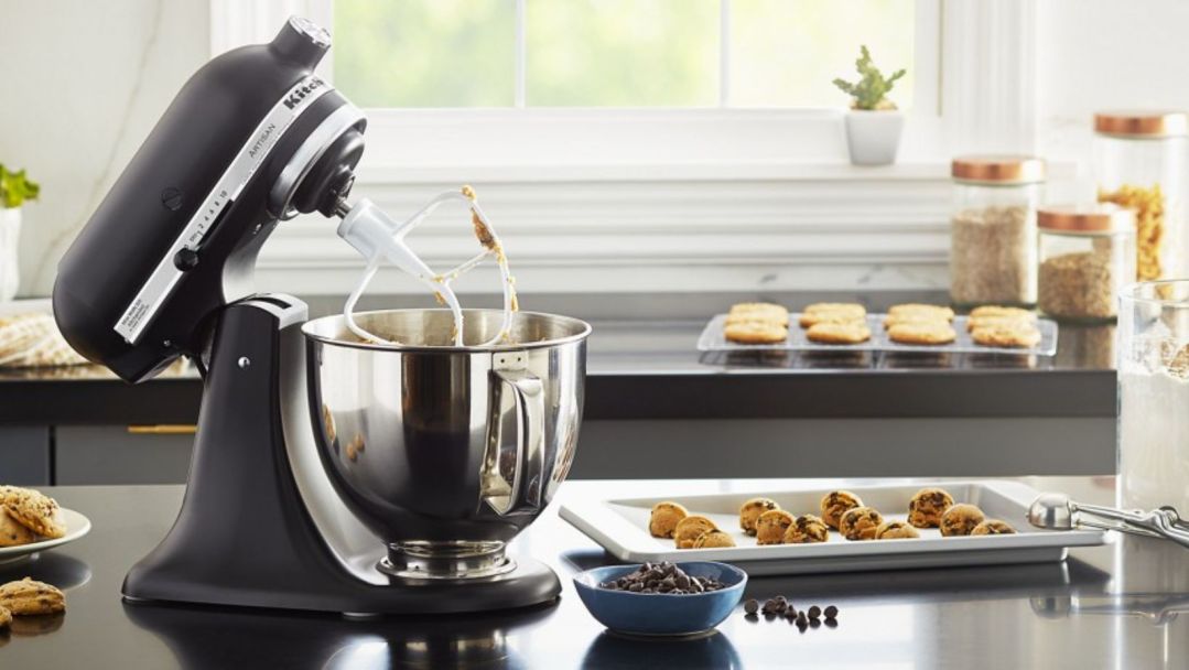 An image of A black kitchenaid mixer on a counter with ingredients for chocolate chip cookies surrounding it
